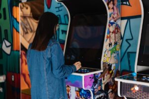 A woman with long hair plays a retro arcade game indoors, enjoying classic gaming fun.